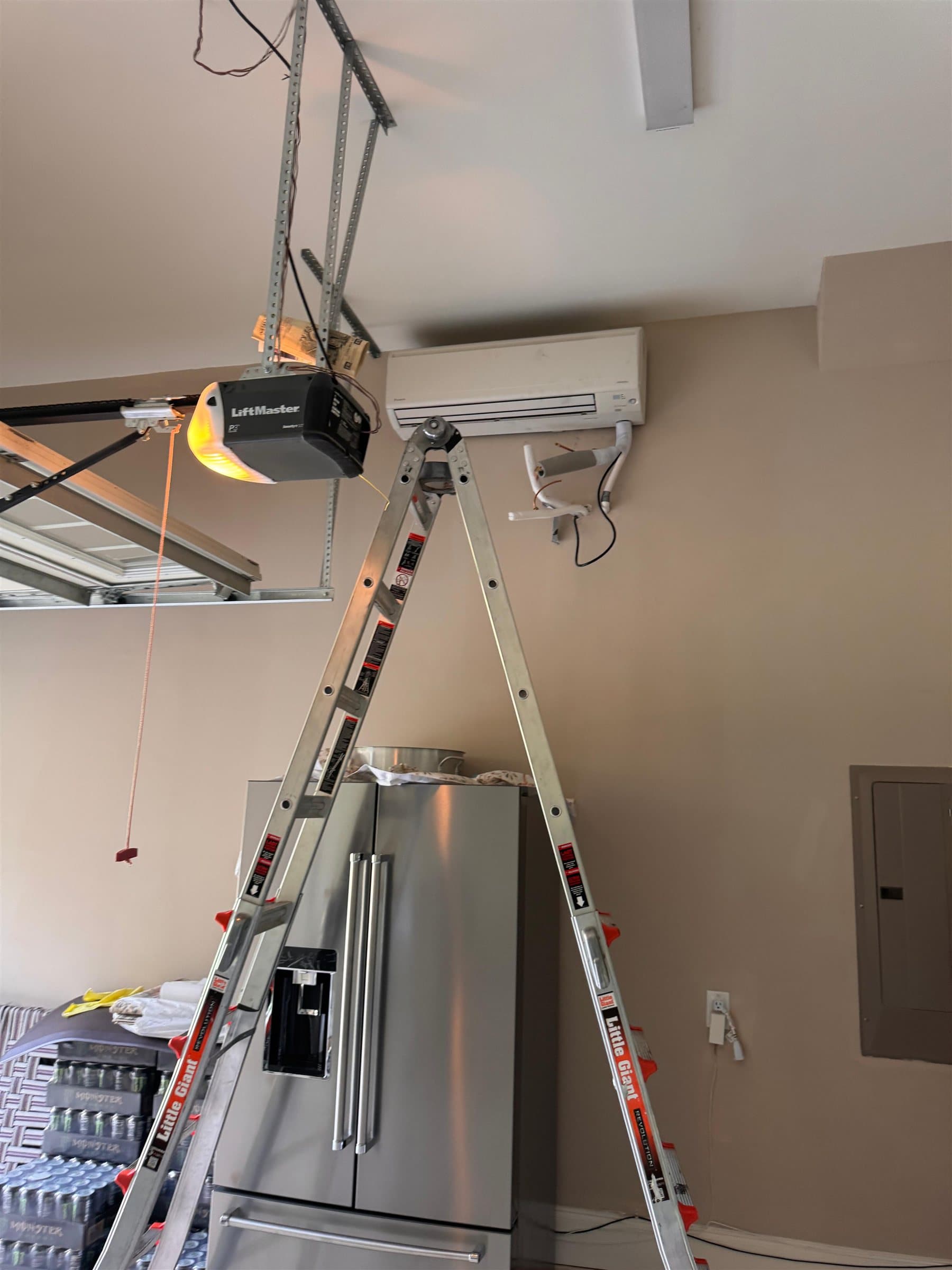 Ductless mini-split indoor unit mounted high on a garage wall, with a stepladder set up beneath it.