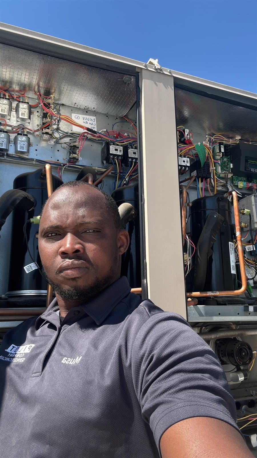 The owner of FMA Industries in a company polo, standing in front of an open commercial rooftop unit.